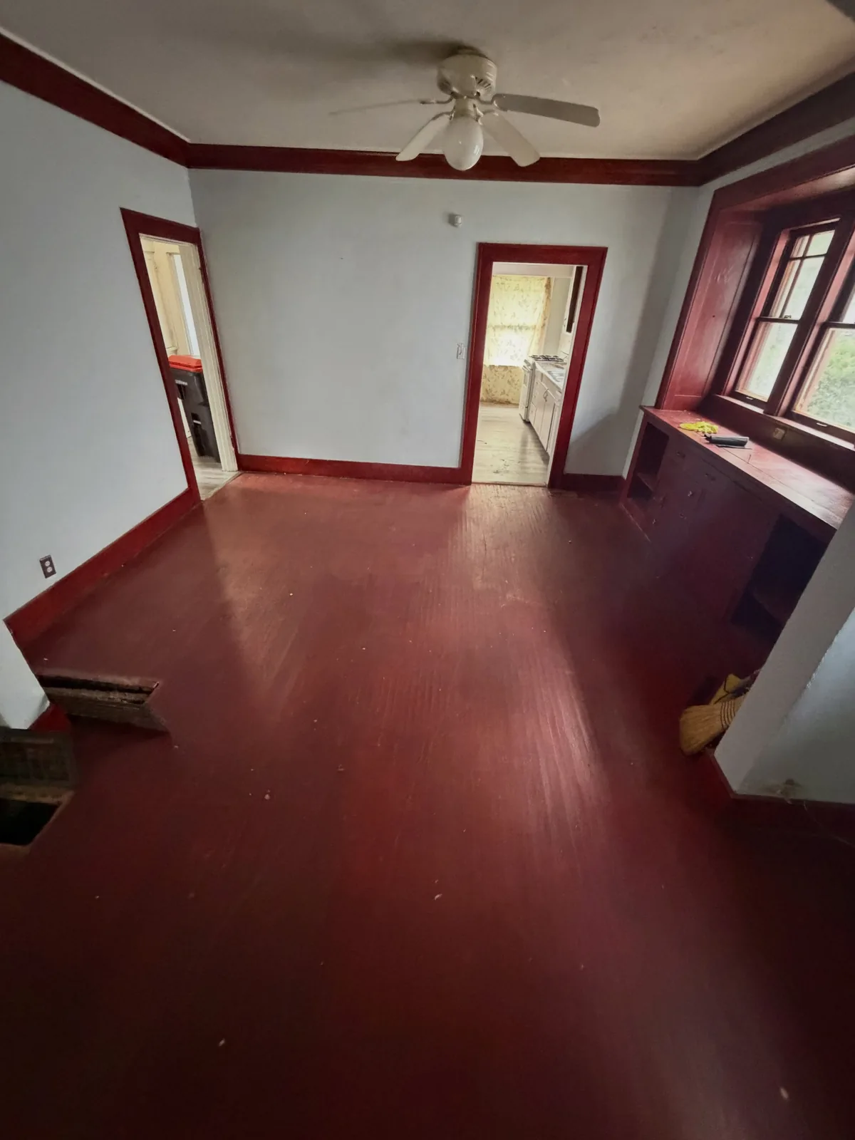 Same living room emptied and swept down to bare red hardwood after cleanout