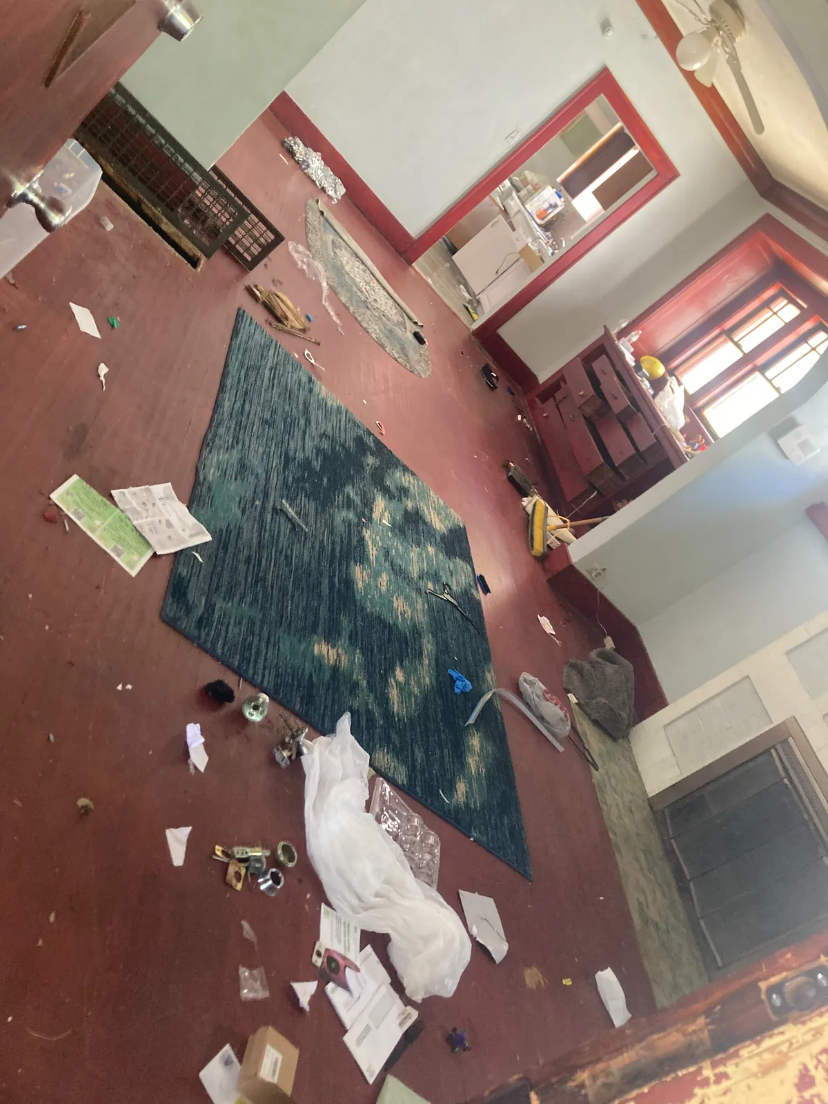 Red hardwood living room strewn with an old area rug and belongings left behind before cleanout